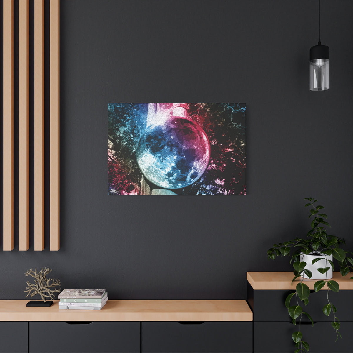 Universe in a Mirror canvas on a charcoal wall over an oak shelf, moon-like orb in blue and pink film tones in a surreal sky