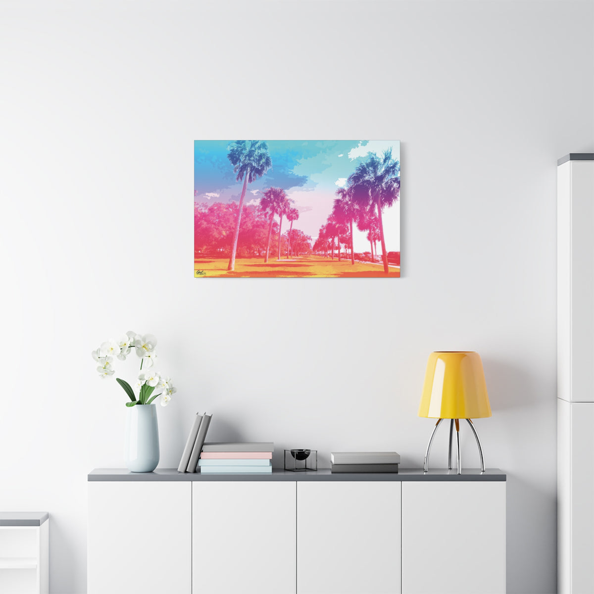 The Battery Tropical Edition small canvas above a white sideboard and yellow lamp, palms in a pink and turquoise sunset