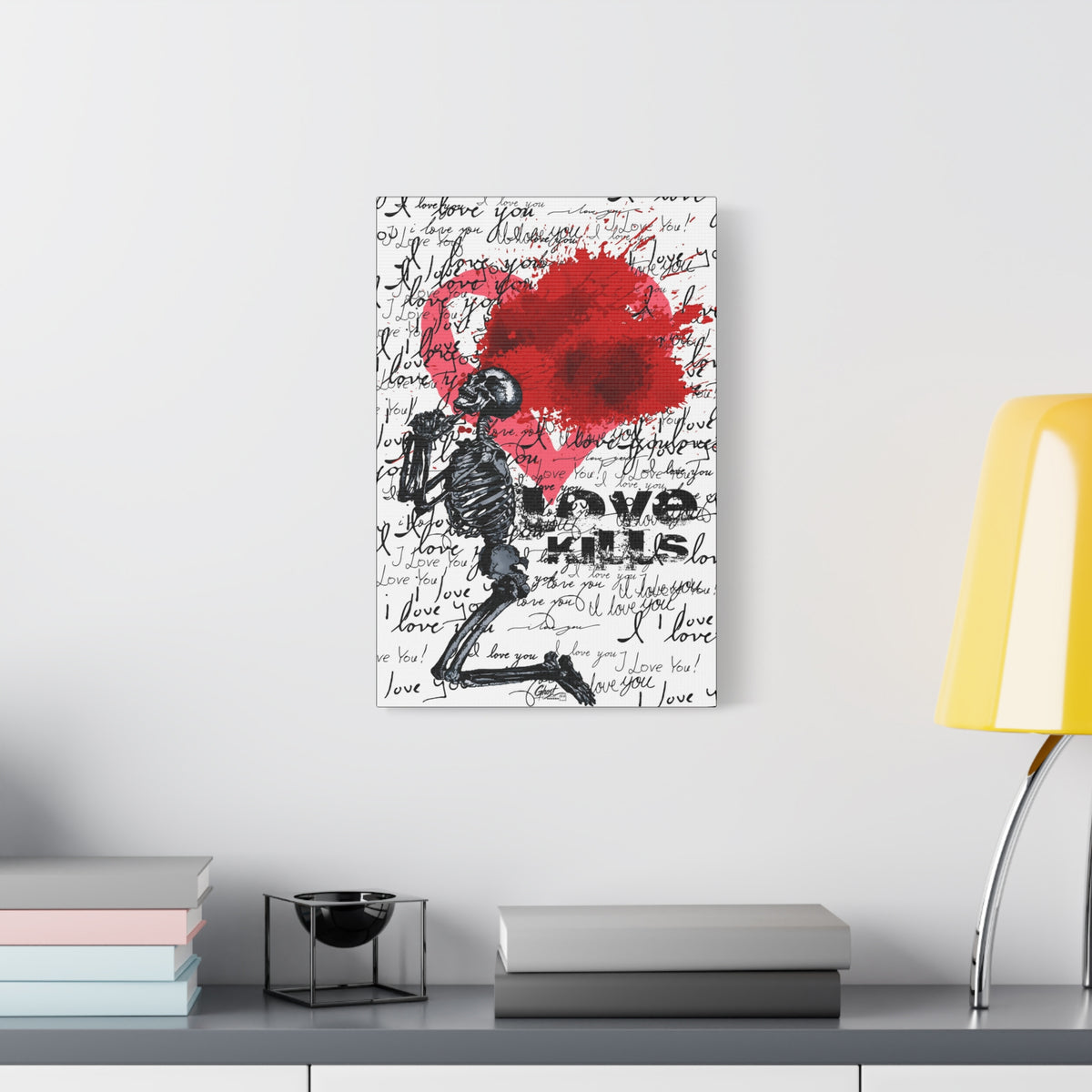 Love Kills medium canvas beside a yellow desk lamp, kneeling skeleton before a burst pink and crimson heart