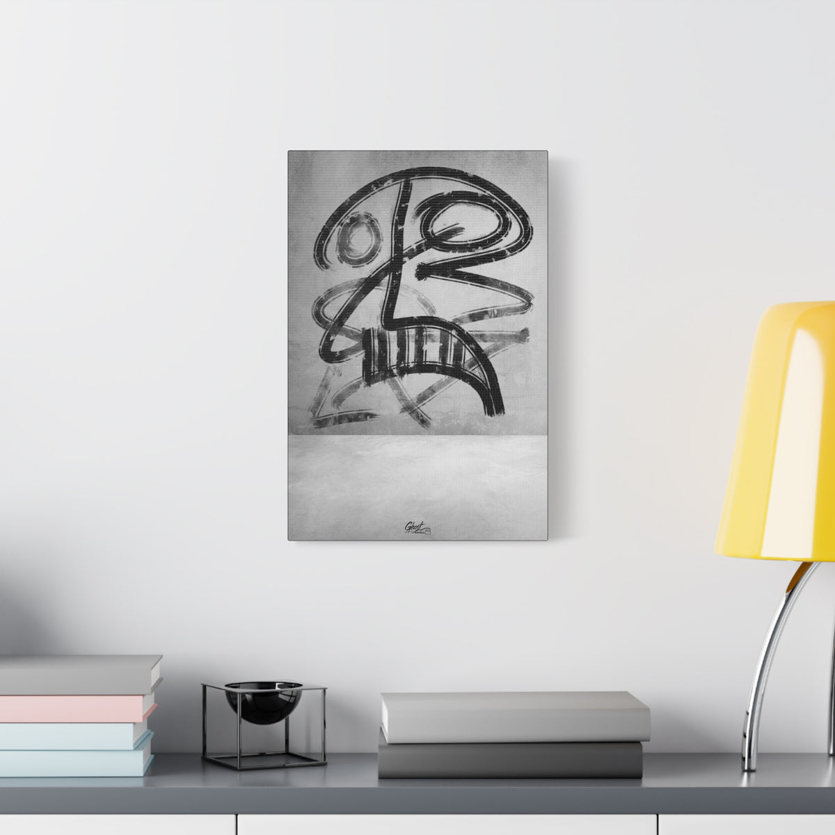 The Mask small canvas beside a yellow desk lamp, bold black brushstroke mask-like figure on a gray field