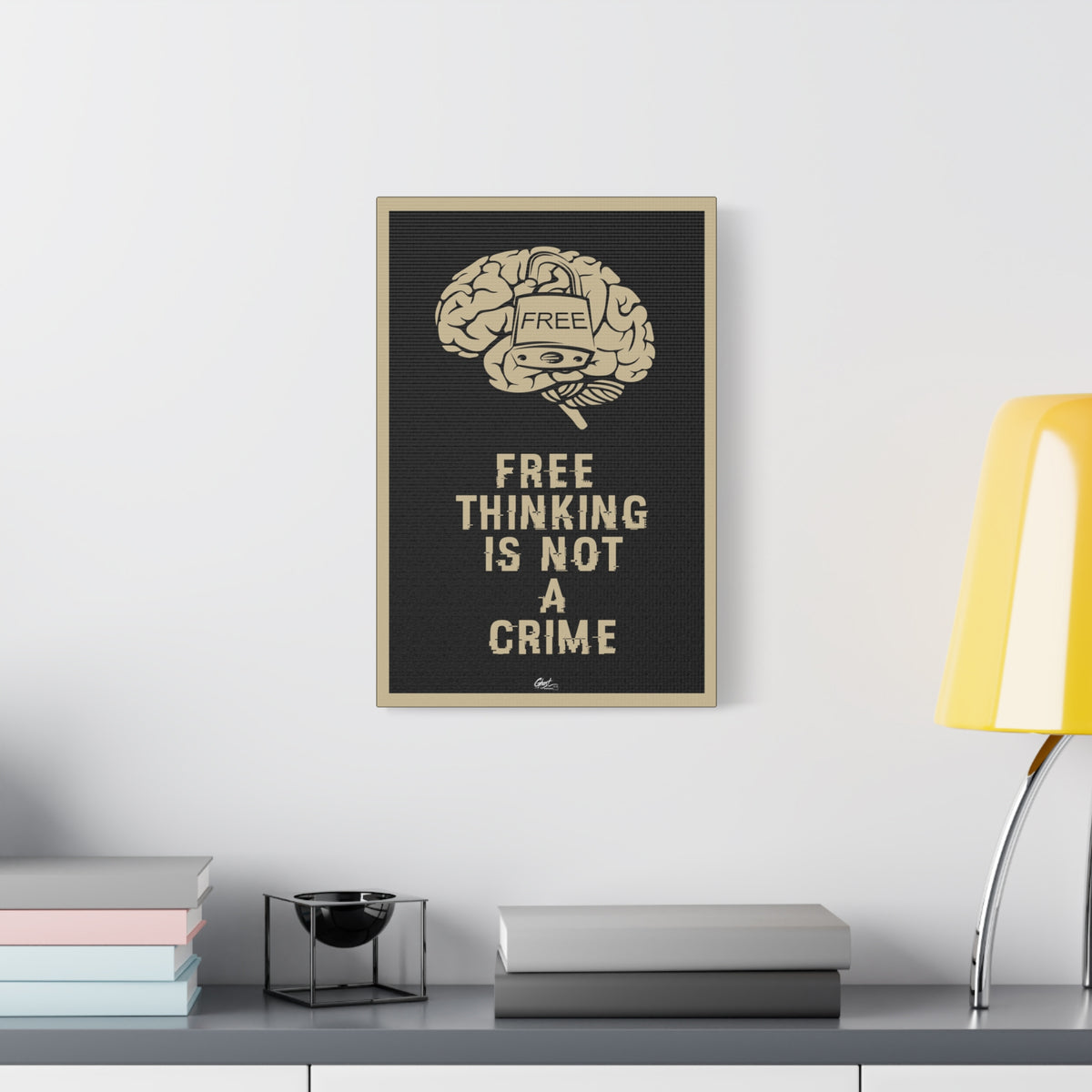 Free Thinking Is Not a Crime canvas beside a yellow desk lamp, locked brain with a padlock stamped Free, beige on charcoal