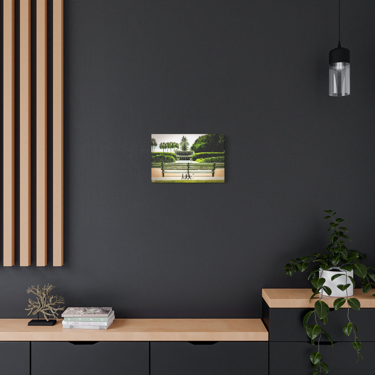 Pineapple Crossing canvas on a charcoal wall over an oak shelf, painterly park scene with the pineapple fountain