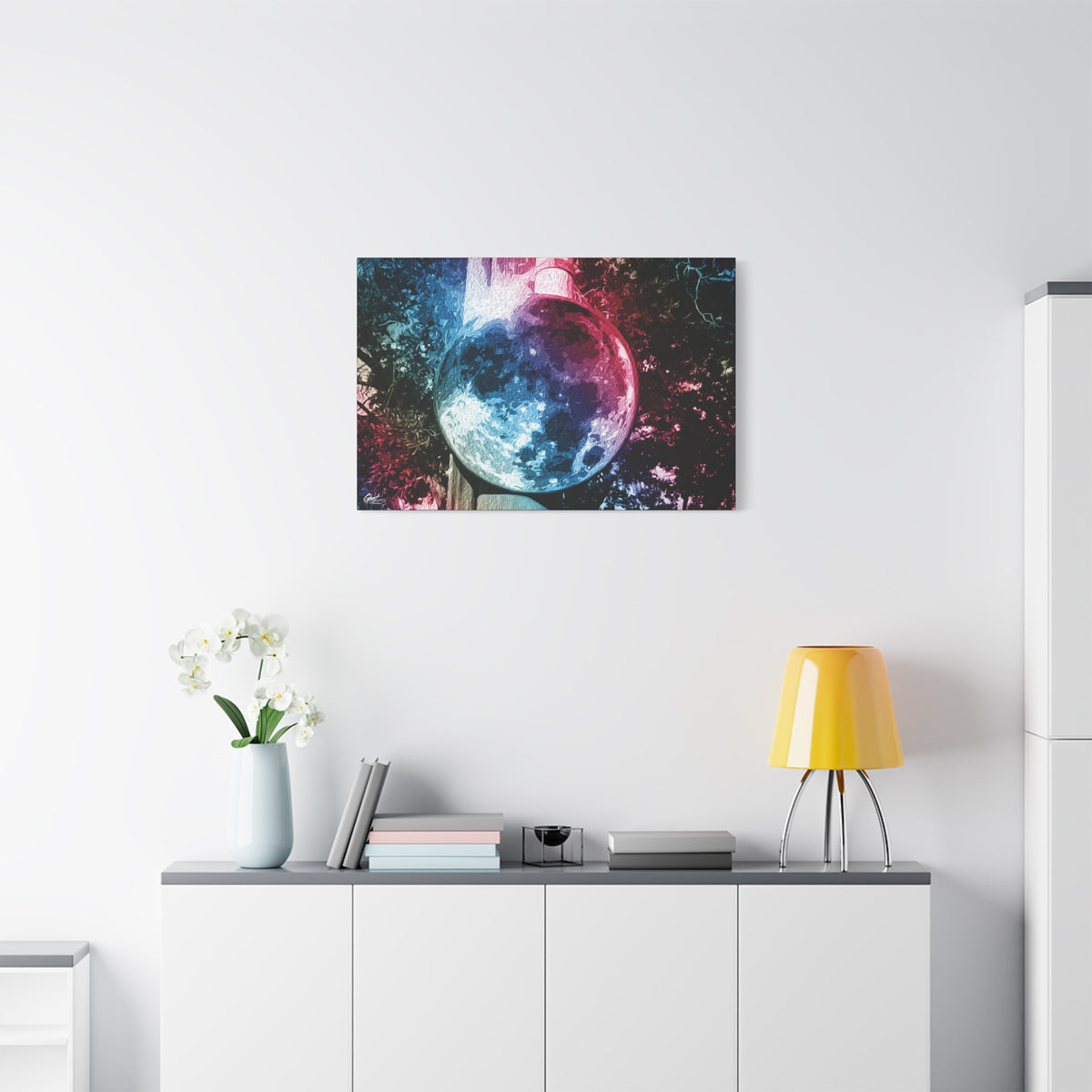 Universe in a Mirror canvas above a white sideboard and yellow lamp, glowing mirrored orb floating in a dreamy pink-blue sky