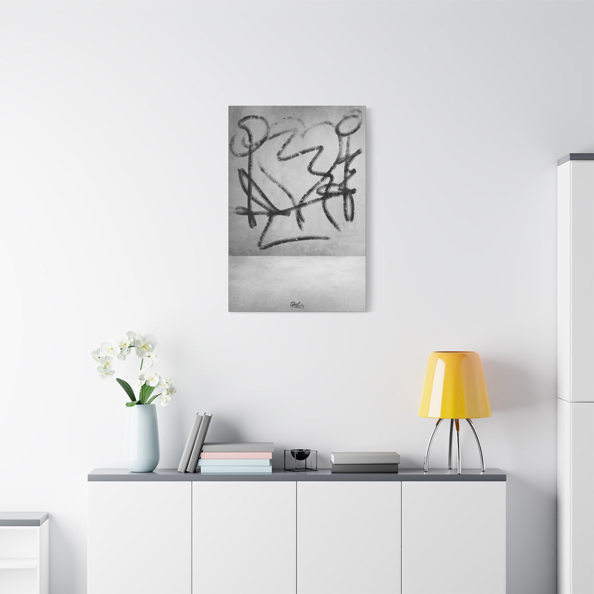 Heartbreak canvas above a white sideboard and yellow lamp, broad black charcoal-style strokes over a pale textured ground