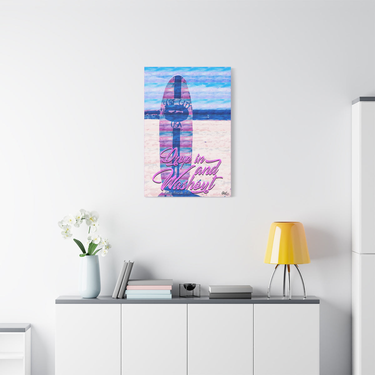 Drop In and Wash Out, Folly Beach canvas above a white sideboard and yellow lamp, pastel surfboard with script lettering